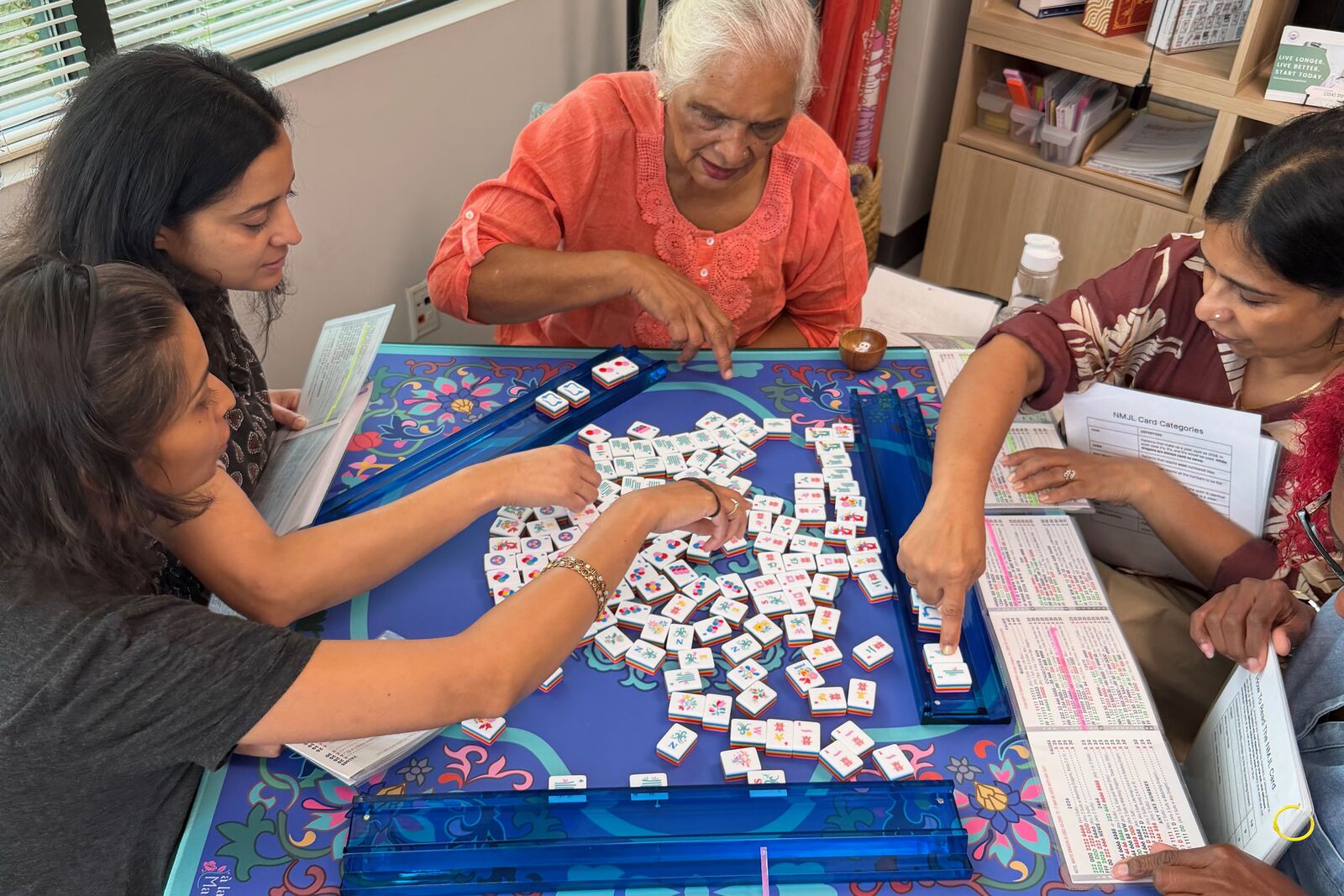 A Mahjong 101 group leaning in over the table, sorting tiles together during a guided lesson